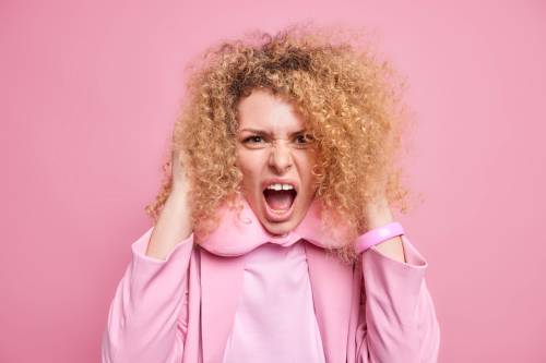 outraged mad young woman with curly hair screams loudly being very angry keeps mouth opened wears travel pillow around neck formal clothes isolated pink wall human emotions concept 7 نکته مراقبت از موی خشک